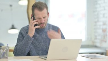 Displeased Mature Adult Man Talking Angrily on Smartphone at Work