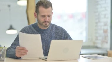 Mature Adult Man Celebrating Success while Working on Laptop and Documents