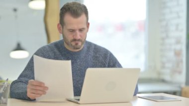 Mature Adult Man Feeling Upset while Working on Laptop and Documents