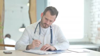 Doctor Working on Medical Report and Laptop in Clinic