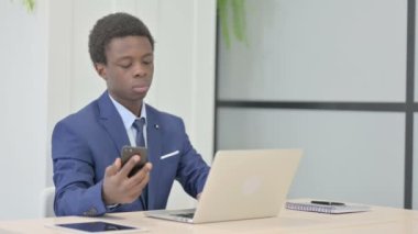 African Businessman using Smartphone while using Laptop