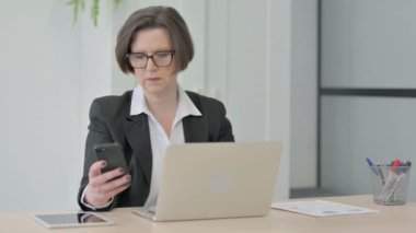 Old Senior Businesswoman using Smartphone while using Laptop