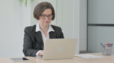 Dizüstü bilgisayar kullanırken kameraya gülümseyen yaşlı iş kadını