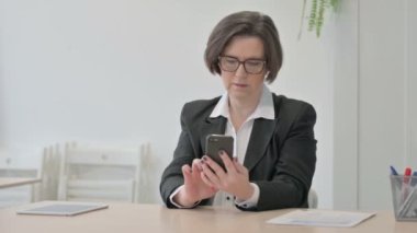 Old Senior Businesswoman Browsing Internet on Smartphone in Office