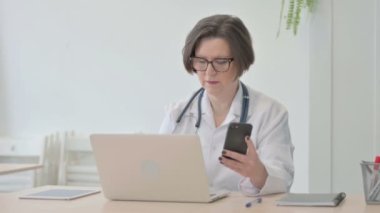 Old Senior Doctor using Smartphone while using Laptop