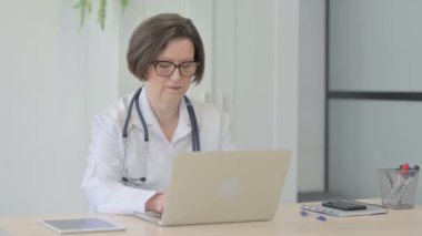Senior Female Doctor Shaking Head in Rejection while Working on Laptop