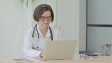 Senior Female Doctor Smiling at Camera while using Laptop