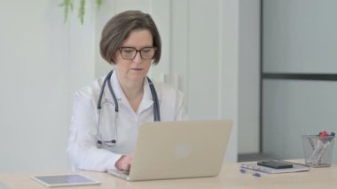 Senior Female Doctor Looking at Camera while using Laptop