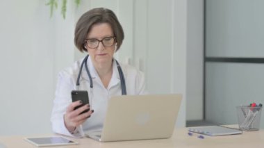 Üst düzey kadın doktor dizüstü bilgisayar kullanırken Smartphone kullanıyor