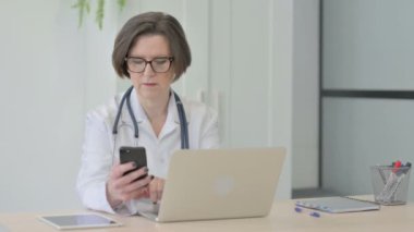 Senior Female Doctor Talking on Phone while using Laptop
