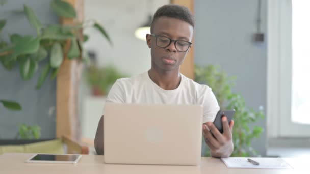 Hombre Africano Usando Smartphone Mientras Usa Laptop — Vídeo de stock