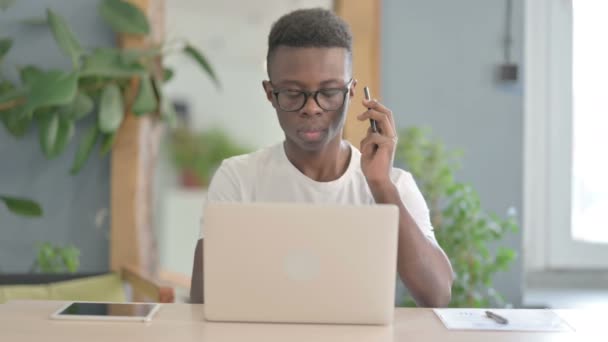 非洲男人一边打电话一边用笔记本电脑 — 图库视频影像