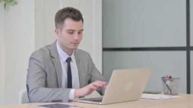 Young Businessman Smiling at Camera while using Laptop