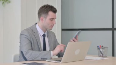 Displeased Young Businessman Talking Angrily on Smartphone at Work