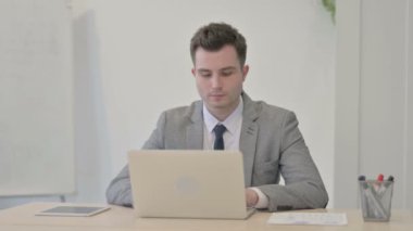 Young Businessman Smiling at Camera while using Laptop