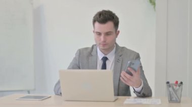 Genç İşadamı dizüstü bilgisayar kullanırken Smartphone kullanıyor