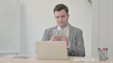 Young Businessman Counting Dollar while Working on Laptop
