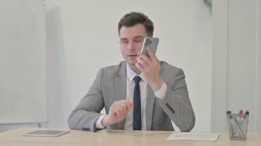 Angry Young Businessman Talking on Smartphone at Work