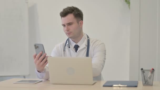 Młody Lekarz Rozmawiający Przez Telefon Podczas Korzystania Laptopa — Wideo stockowe