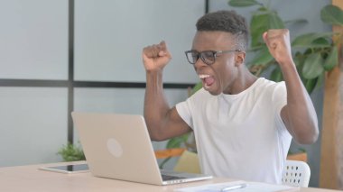 Young African Man Celebrating Online Success on Laptop