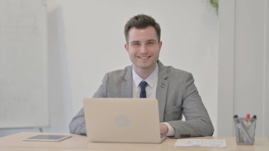 Young Businessman Smiling at Camera while using Laptop