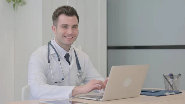 Młody Lekarz Uśmiechnięty Kamery Podczas Korzystania Laptopa — Zdjęcie stockowe