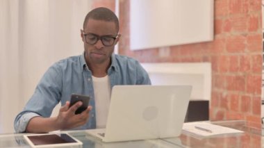 Laptop 'ta çalışan ve akıllı telefon kullanan Afrikalı adam.