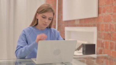 Boyun ağrısı olan genç bir kadın dizüstü bilgisayarda çalışıyor.