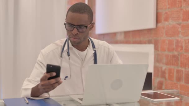 Laptop Üzerinde Çalışan Akıllı Telefon Kullanan Genç Afrikalı Doktor — Stok video