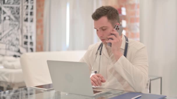 Médico Masculino Conversando Telefone Enquanto Trabalhava Laptop Clínica — Vídeo de Stock