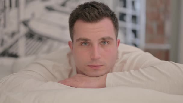 Schwerer Junger Mann Liegt Bett Auf Bauch Und Blickt Kamera — Stockvideo