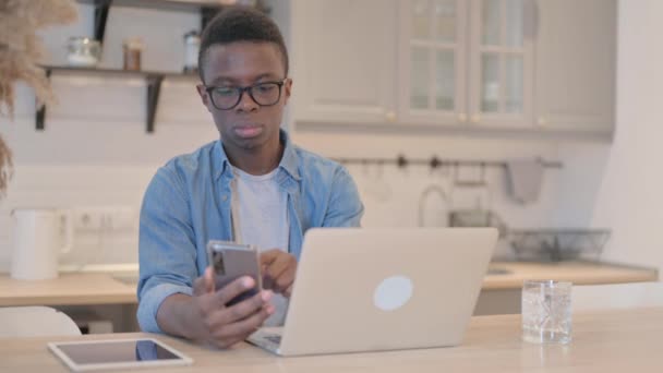 Ung Afrikansk Mann Som Arbeider Laptop Bruker Smartphone – stockvideo