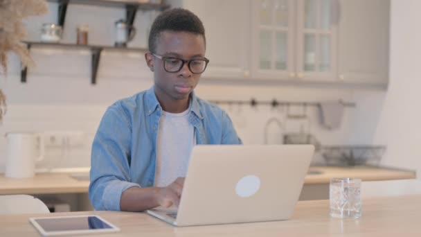 年轻的非洲人一边在相机前微笑一边在笔记本电脑上工作 — 图库视频影像