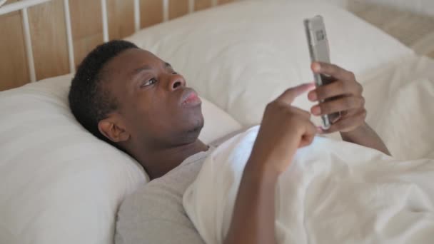 Joven Africano Celebrando Éxito Teléfono Mientras Está Acostado Cama — Vídeos de Stock