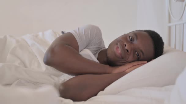 笑顔の若いアフリカ人男性が横にベッドに横たわっている — ストック動画