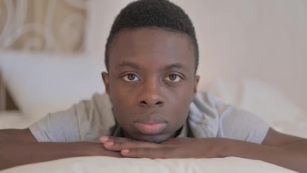 Σοβαρός Νεαρός Αφρικανός Ξαπλωμένος Στο Κρεβάτι Στο Στομάχι Κοιτάζοντας Στην — Αρχείο Βίντεο