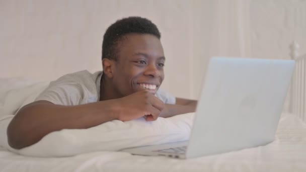 Ung Afrikansk Man Gör Videochatt Laptop Medan Ligger Mage Sängen — Stockvideo