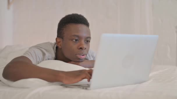 非洲年轻人躺在床上 躺在笔记本电脑上庆祝成功 — 图库视频影像