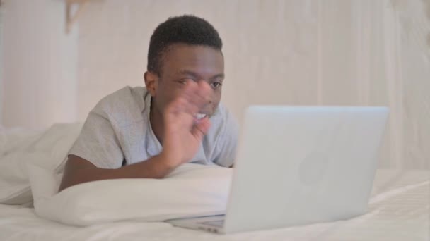 ベッドで胃の上に横たわっている間 若いアフリカ人男性はノートパソコンでビデオチャットを行う — ストック動画