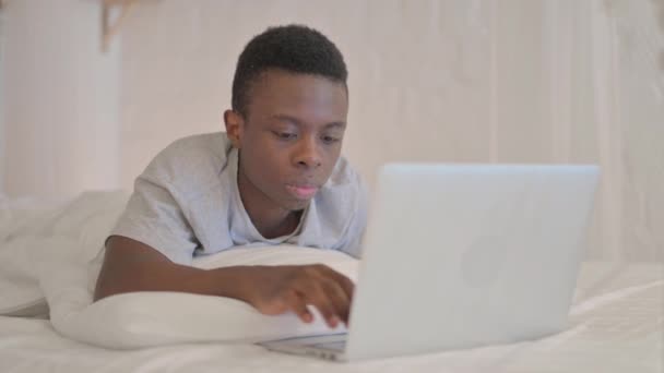 Młody Afrykanin Zszokowany Stratą Laptopie Podczas Leżenia Brzuchu Łóżku — Wideo stockowe