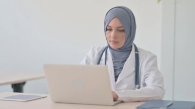 Bilgisayarda çalışırken kameraya gülümseyen Müslüman Kadın Doktor