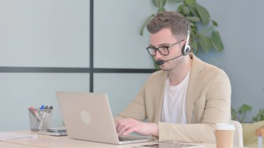 Kulaklıklı genç adam laptopta çalışıyor.