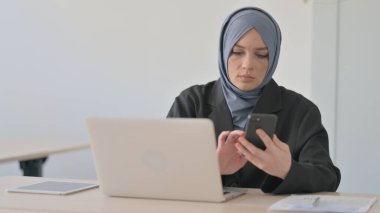 Dizüstü bilgisayarda çalışan ve akıllı telefon kullanan Müslüman İş kadını