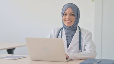 Bilgisayarda çalışırken kameraya gülümseyen Müslüman Kadın Doktor