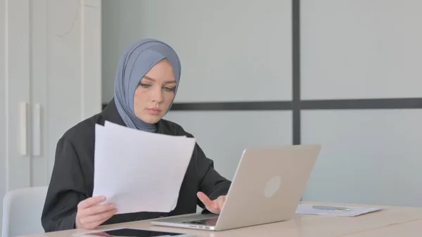 穆斯林女商人和在笔记本电脑上工作的阅读文件 — 图库照片