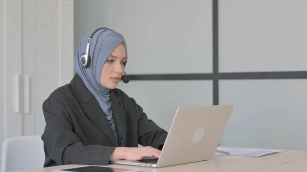 戴耳机在笔记本电脑上工作的穆斯林女商人 — 图库照片