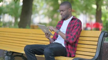 Tablet kullanan genç Afrikalı bir adam Bench 'in üzerinde otururken