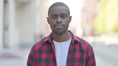 Dudaklarında parmak olan Afrikalı bir gencin açık hava portresi.