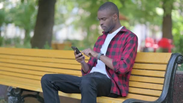 Młody Afrykanin Zszokowany Stratą Smartfonie Podczas Siedzenia Zewnątrz Ławce — Wideo stockowe
