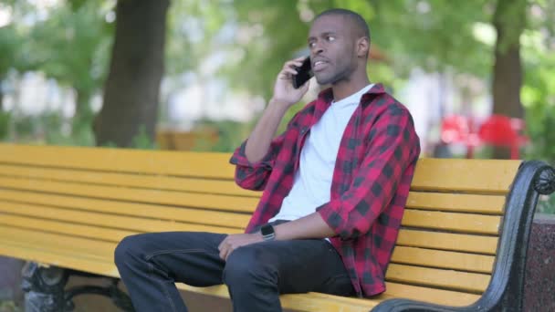 Giovane Africano Parlando Telefono Mentre Seduto All Aperto Una Panchina — Video Stock